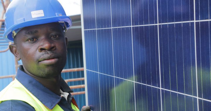 Man posing with solar panels and wearing a hardhat
